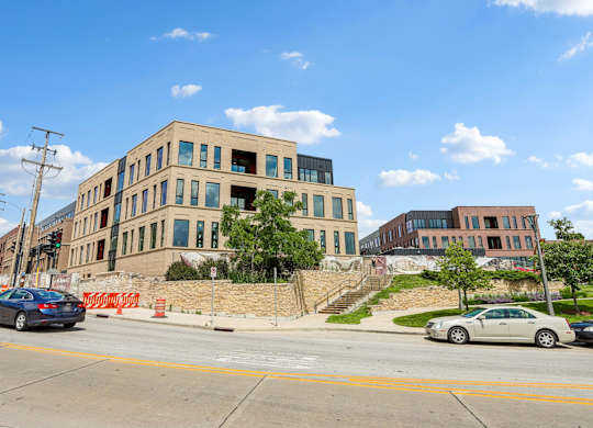 A car is driving on a street past a building with a brown and beige facade.
