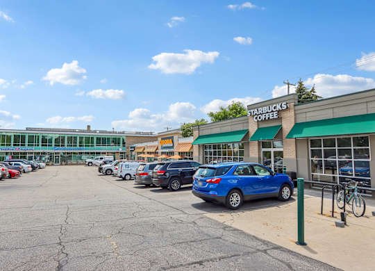 A Starbucks Coffee store with a blue car parked in front.