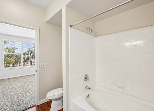 A white bathroom with a tub, toilet and window.