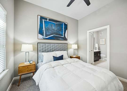 A bedroom with a large bed, a ceiling fan, and a painting on the wall.
