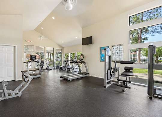 A spacious gym with a variety of equipment and a view of the outdoors through large windows.