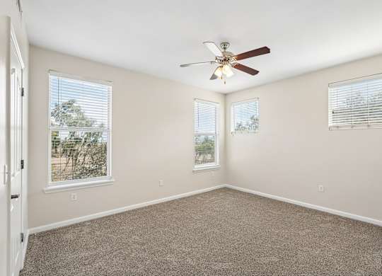 A room with a ceiling fan and two windows.