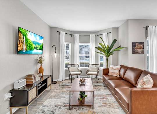 A living room with a brown leather couch, a coffee table, and a flat screen TV mounted on the wall.