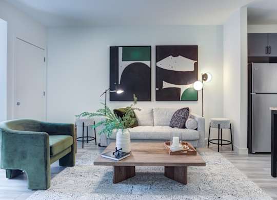 A living room with a green chair, a white couch, and a painting on the wall.