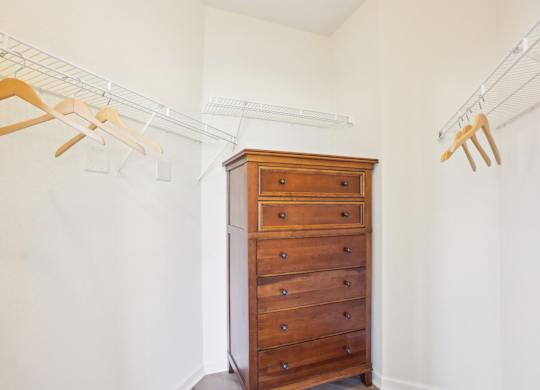 A wooden chest of drawers with clothes hanging on a rail above it.