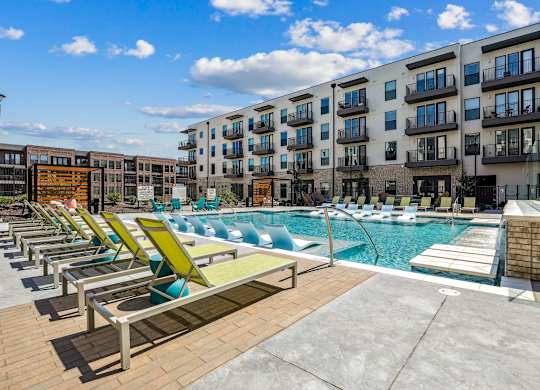 A sunny day at the poolside with lounge chairs and apartment buildings in the background.