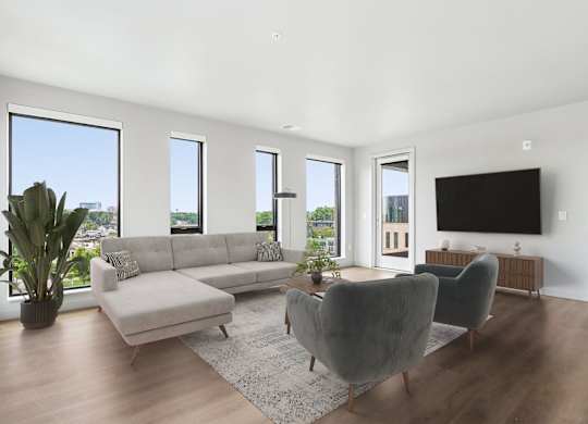 A living room with a grey couch, a grey chair, a grey ottoman, a television, and a potted plant.