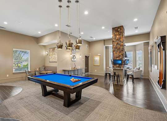 A pool table is in the middle of a room with a wood floor and a stone pillar.
