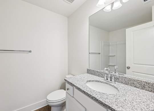 A bathroom with a toilet, sink, mirror, and towel rack.