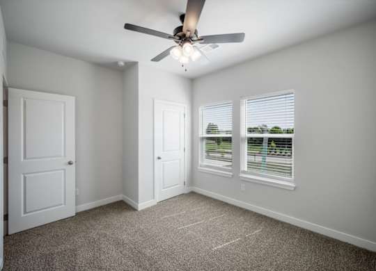 A room with a ceiling fan and two windows.