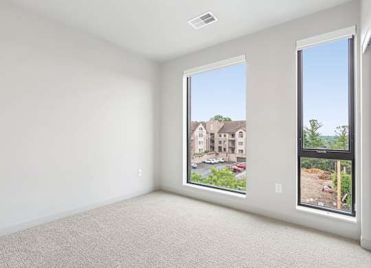 A large empty room with a view of a building and trees outside the window.