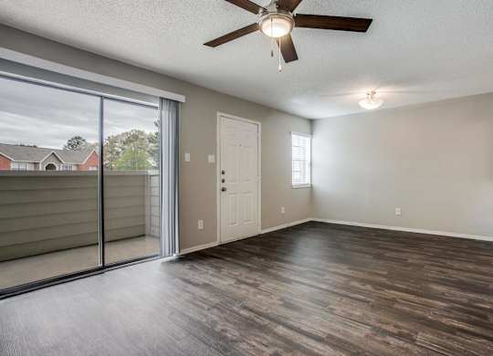 an empty living room with a sliding glass door and a ceiling fan