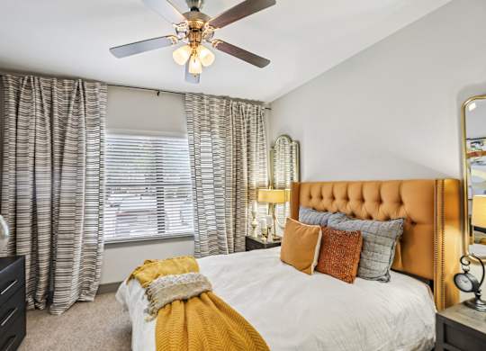 A bedroom with a bed, a dresser, a ceiling fan, and a window with curtains.
