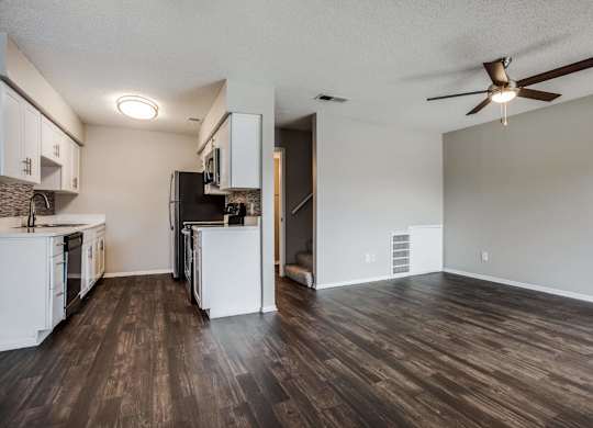 an empty living room with a kitchen and a ceiling fan