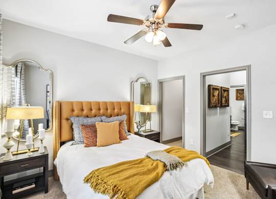 A bedroom with a bed, a ceiling fan, and a mirror.