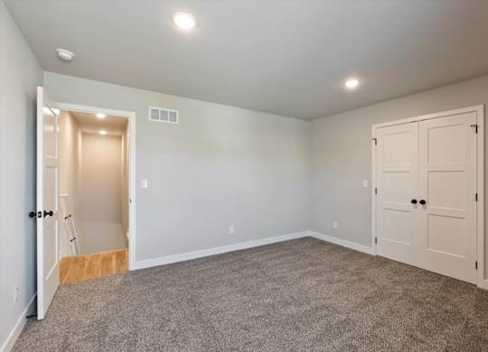 A room with a carpeted floor and two doors, one of which is open.