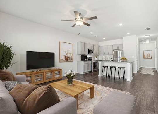 A modern living room with a flat screen TV, a coffee table, and a kitchen area in the background.