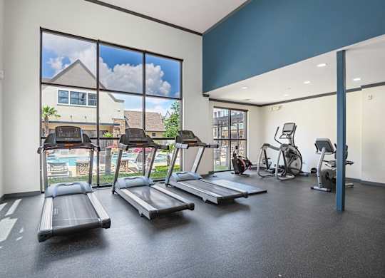 A gym with treadmills, exercise bikes, and a view of a pool and houses outside.
