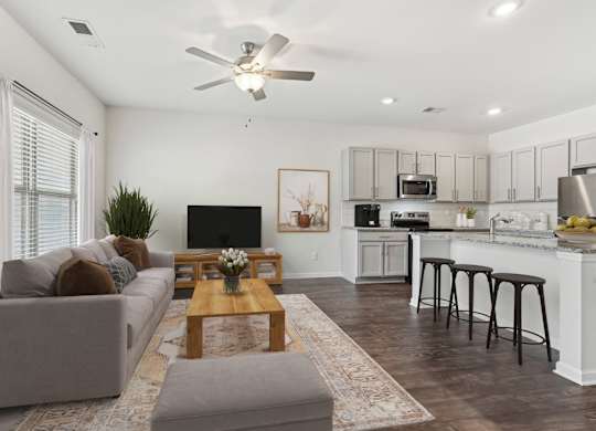 A modern living room with a grey couch, a wooden coffee table, and a kitchen area in the background.