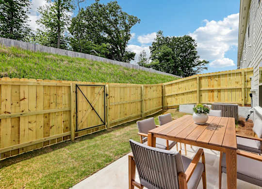 A wooden fence encloses a backyard with a table and chairs.