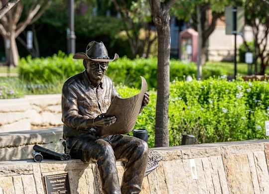 A statue of a man reading a book sits on a bench.