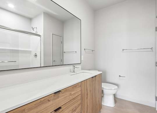 A white toilet sits in a bathroom with a wooden vanity and a large mirror.