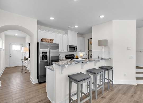A kitchen with a refrigerator, stove, and bar stools.