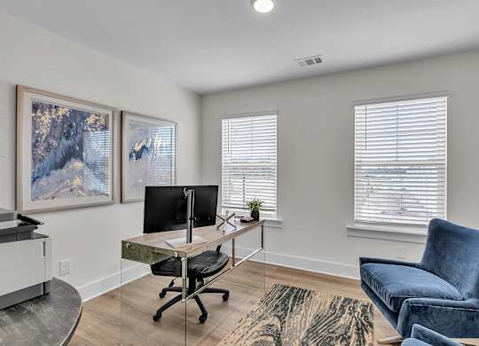 A room with a desk, chair, and two framed pictures on the wall.