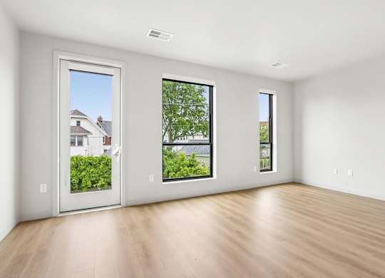 A room with a wooden floor and three windows showing the outdoors.