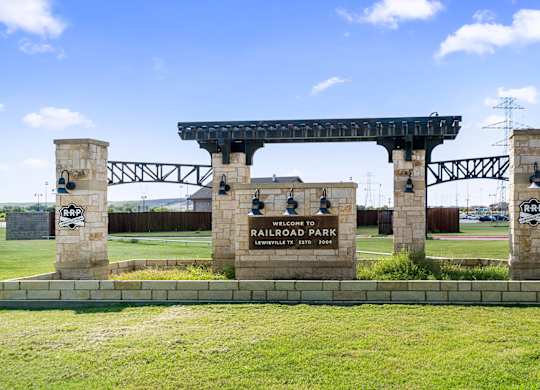 A sign welcoming visitors to Railroad Park stands in front of a bridge.
