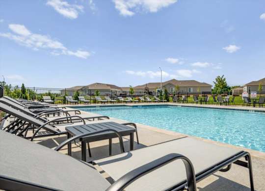 A pool with sun loungers and a fence in the background.