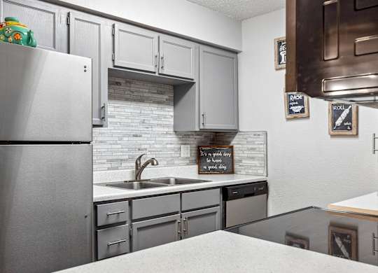 A kitchen with a refrigerator, sink, and cabinets.