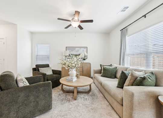 A living room with a grey couch, a brown armchair, a coffee table, and a ceiling fan.