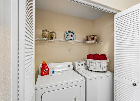A laundry room with a washer and dryer, a basket of red balls, and a shelf with jars and a sign that says