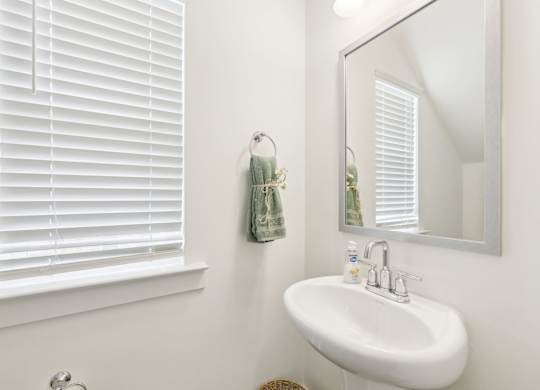 A white sink in a bathroom with a mirror and a window with blinds.
