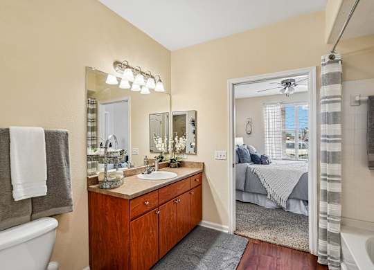 A bathroom with a white tub, a wooden vanity, and a bedroom in the background.