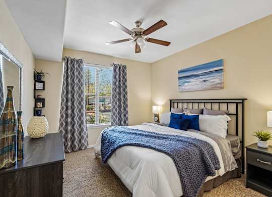 A bedroom with a large bed, a ceiling fan, and a painting on the wall.
