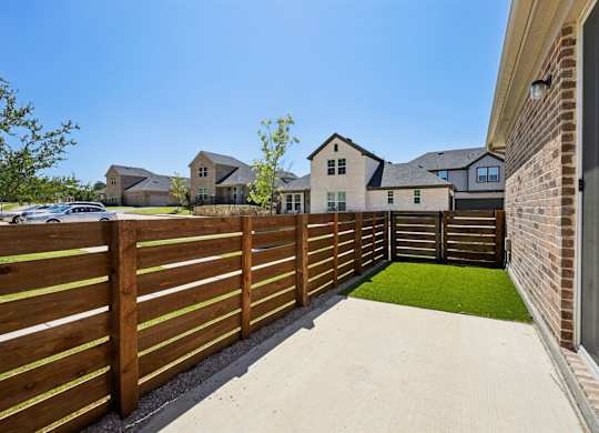 A wooden fence separates a house from a green lawn.