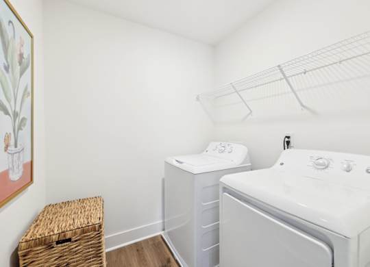A laundry room with a washer and dryer, a basket, and a painting on the wall.