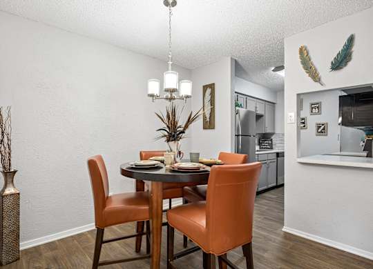 A dining room with a table set for two and a kitchen in the background.