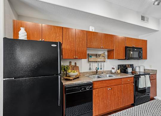 A black refrigerator stands next to a kitchen counter with a sink and a microwave.
