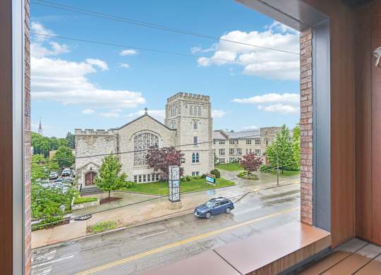 A view from a window looking out at a street with cars and a building with a tower.