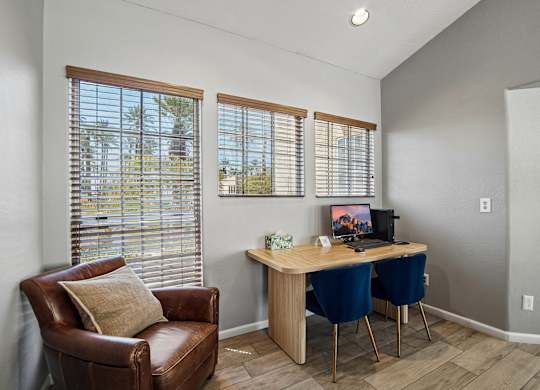 A room with a brown leather chair, a wooden desk with two chairs and a window with blinds.