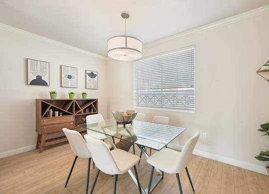 A dining room with a glass table and white chairs.