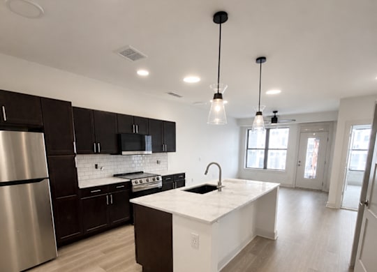 Dog-Friendly Apartments in Kokomo, IN - The Elwood Apartments - Kitchen With Dark Cabinets, Stainless Steel Appliances, A White Island, Pendant Lights, And Luxury Vinyl Plank Flooring.