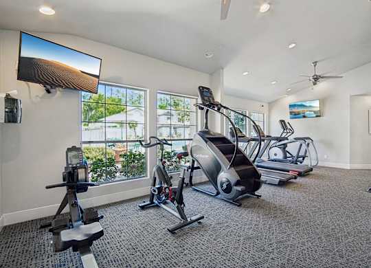 A spacious gym with a variety of equipment including treadmills, elliptical machines, and a television.