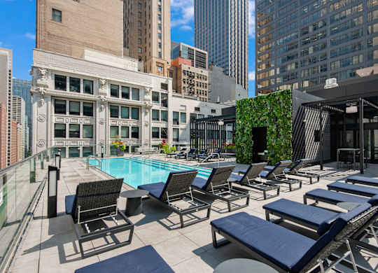 A pool surrounded by chairs and a building in the background.
