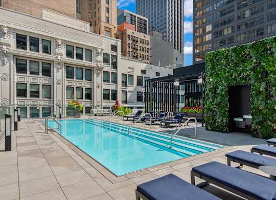 A pool surrounded by chairs and a green wall.