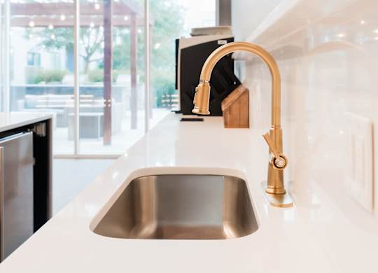 A kitchen sink with a gold faucet and a black dishwasher.