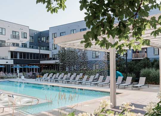 A pool surrounded by chairs and trees with a building in the background.